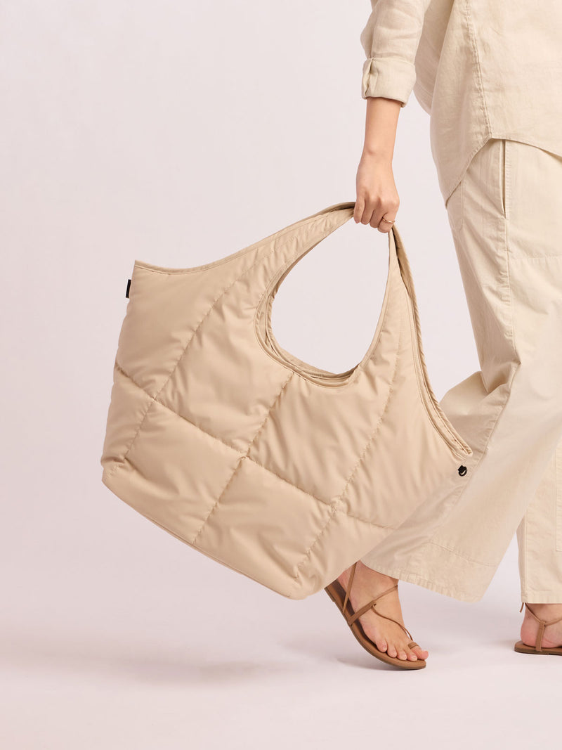 Model holding the CALPAK Luka Everything Tote in off-white beige Oatmeal