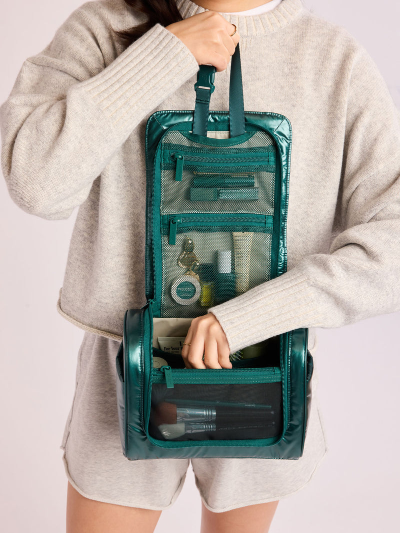 Person adding toiletries in CALPAK Luka Hanging Toiletry Bag in dark green shiny Kale