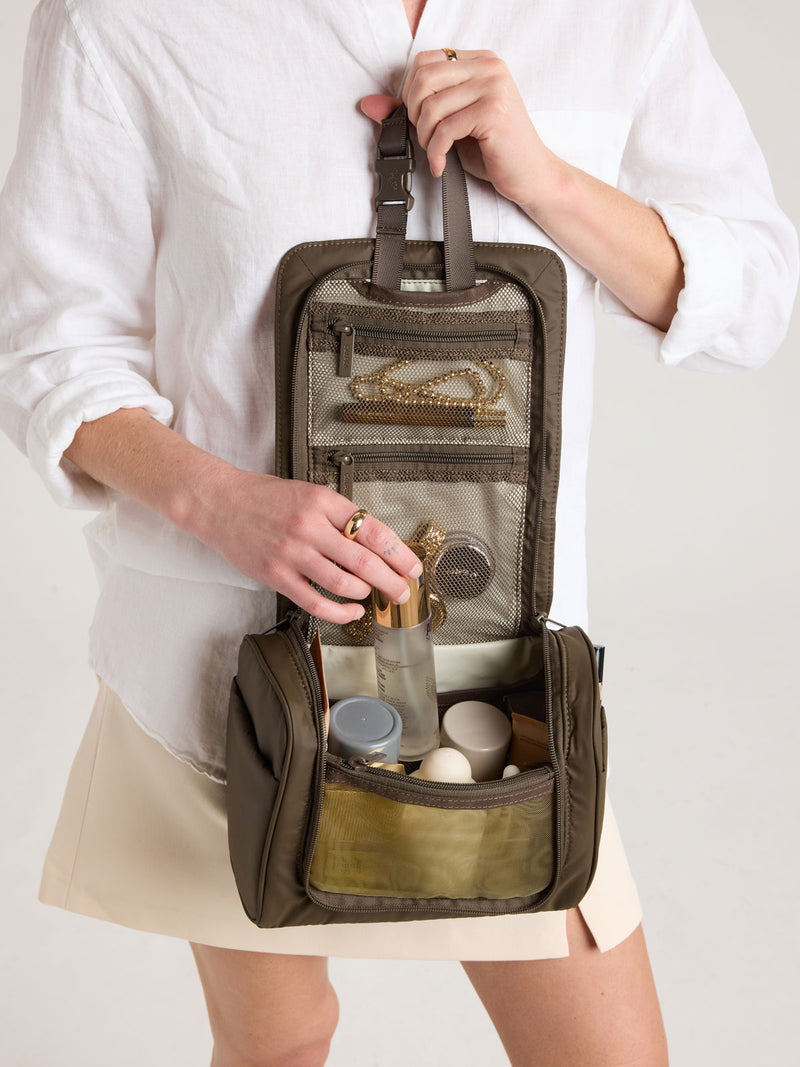 Person adding toiletries into CALPAK Luka Hanging Toiletry Bag in brown Mushroom