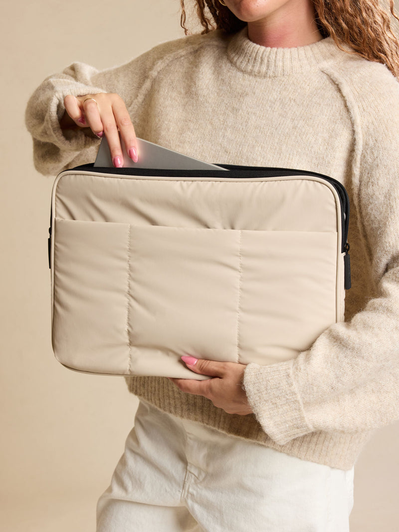 Model holding the CALPAK Luka 17-in Padded Laptop Sleeve in creamy white Oatmeal with puffy exterior back view