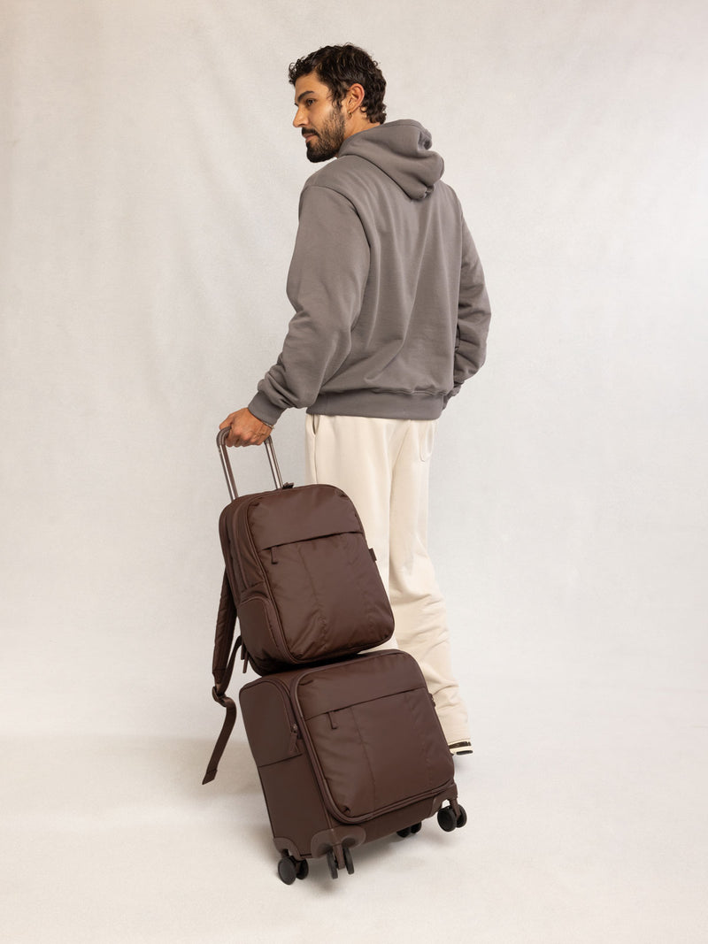 Man holding CALPAK Mini Luka Soft-Sided Carry On Luggage brown Walnut