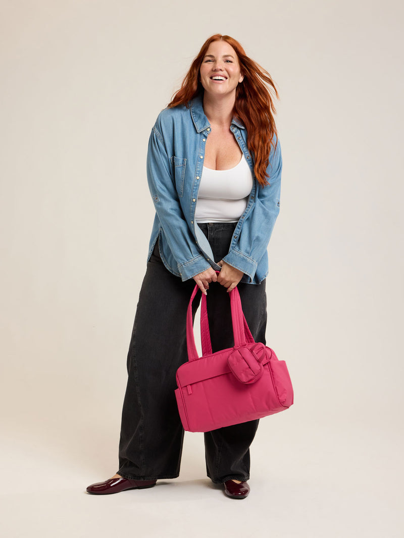 Model holding CALPAK Luka Mini Duffel in bright pink on a white background