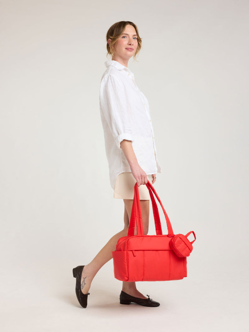 Model holding CALPAK Luka Mini Duffel in red Tomato