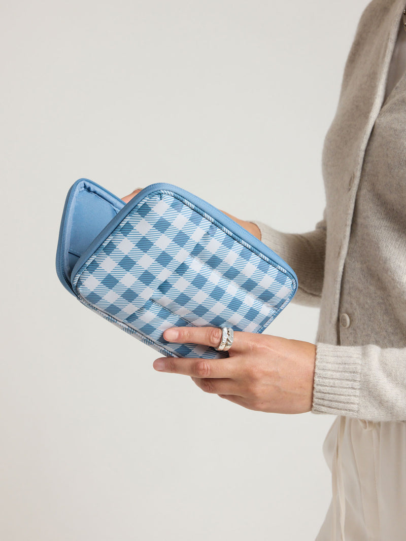 Woman holding the CALPAK Luka Zippered Passport Wallet in white and blue gingham print in French Blue Gingham