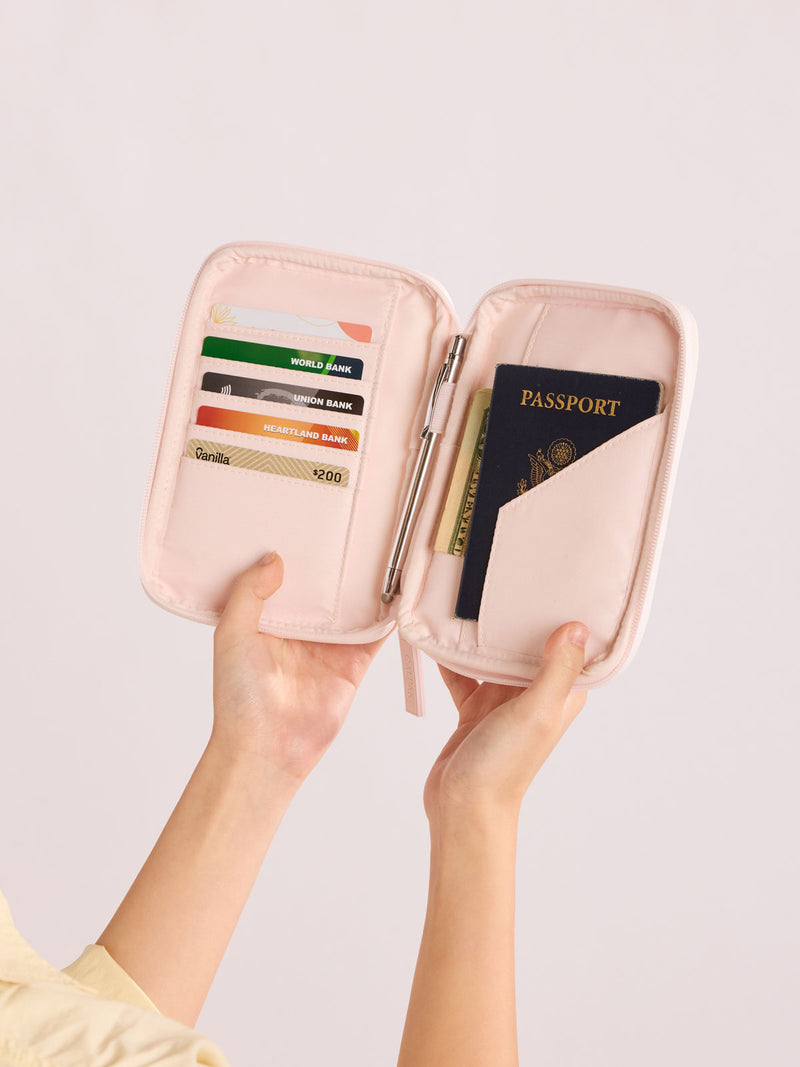 Person holding open CALPAK Luka Zip Passport Wallet in light pink shiny Pearlescent