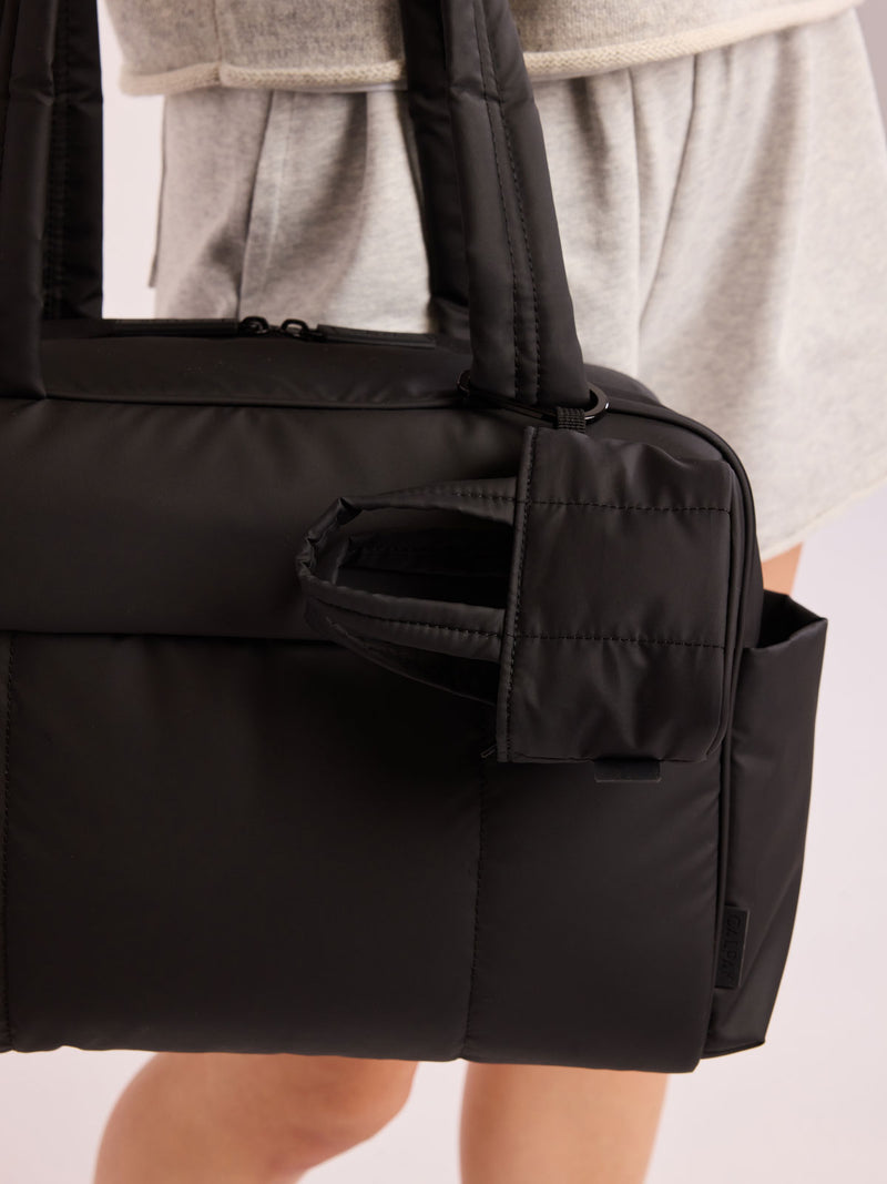 Model holding bag that has the CALPAK Luka Tote Zip Bag Charm in Matte Black with carabiner attached