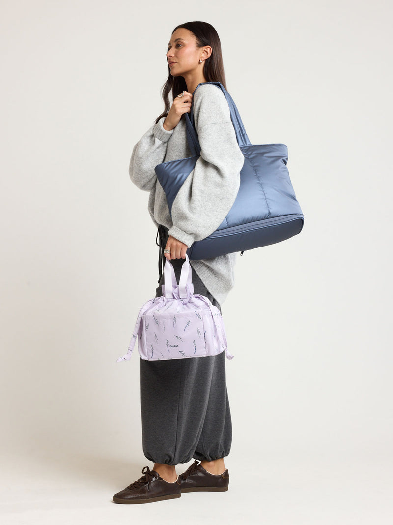 Woman wearing CALPAK Luka Expandable Tote in dark blue metallic material in Metallic Indigo