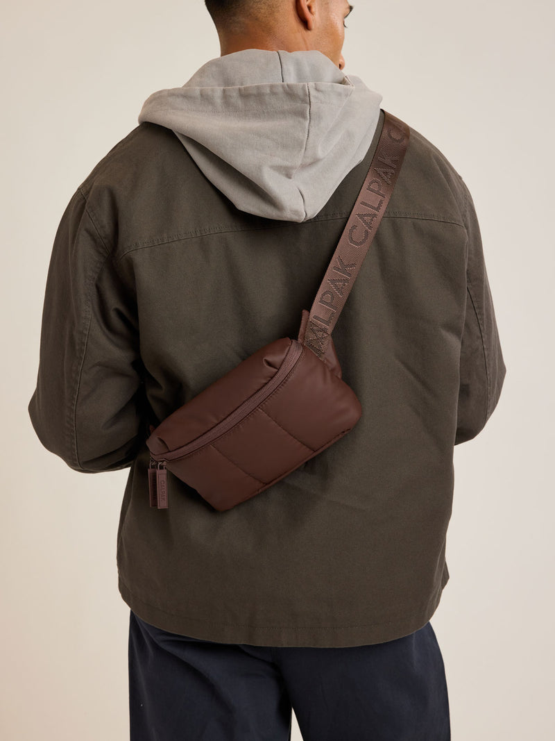 Model wearing CALPAK Luka Mini Belt Bag in brown Walnut on white background