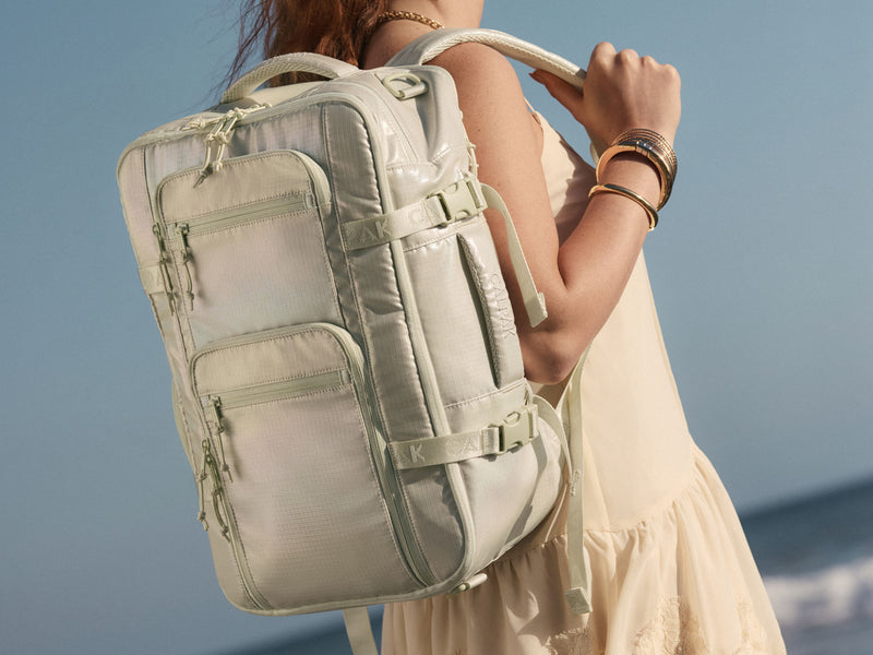 Person wearing a light green Celadon CALPAK Terra 26L backpack against a blue sky background