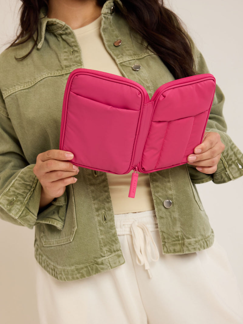 Model holding opened CALPAK Luka Zip Passport Wallet in bright pink Dragonfruit on a white background