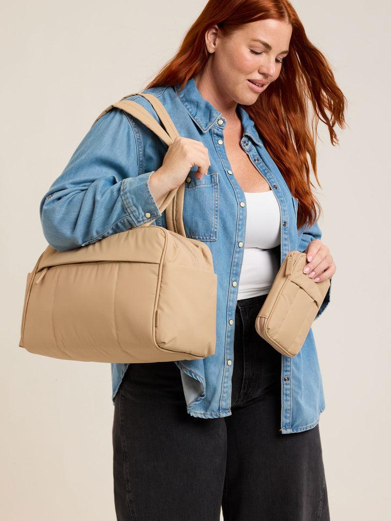 Model holding CALPAK Luka Zip Passport Wallet in beige Latte on a white background