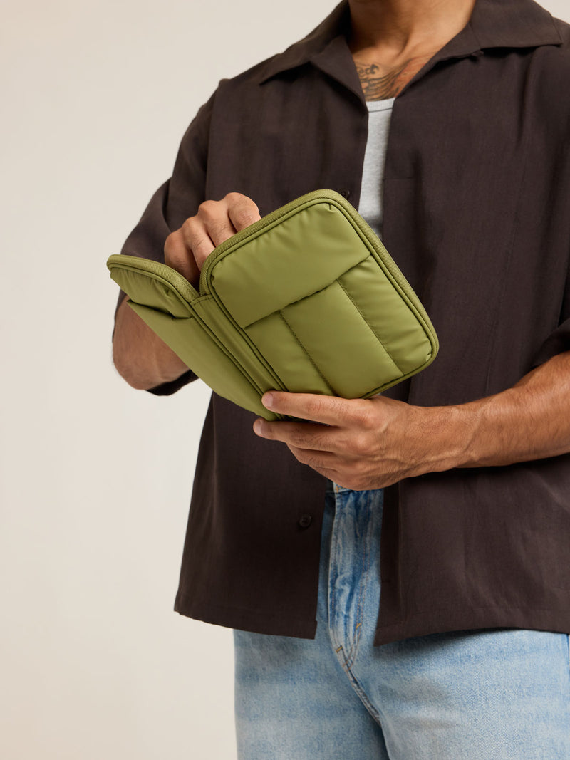 Model holding an opened CALPAK Luka Zip Passport Wallet in dark green Pistachio on a white background