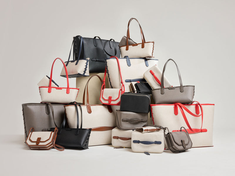 Stack of various CALPAK Colette Collection handbags on a light gray background