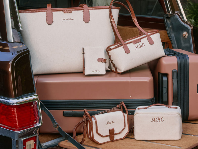 Collection of CALPAK luggage and Colette Collections bags with 'MHC' personalization on a vehicle's open trunk.