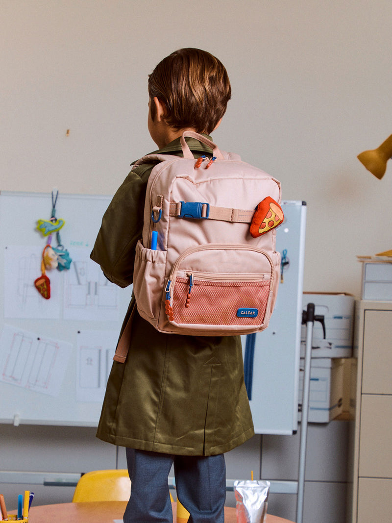 CALPAK Kids Small Backpack in tan/brown Khaki for ages 3-5 being worn by child with a Pizza Pluffy Bag Charm in a classroom