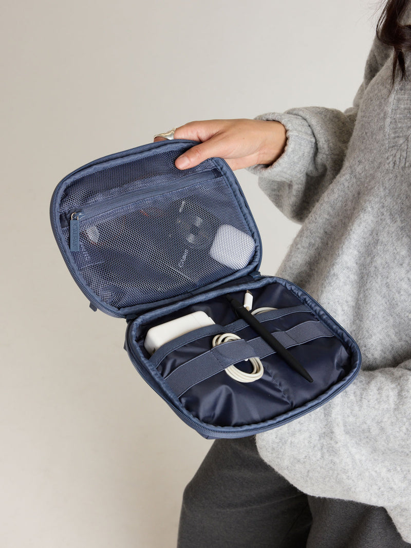 Model opening the CALPAK Tech Organizer in dark blue Indigo