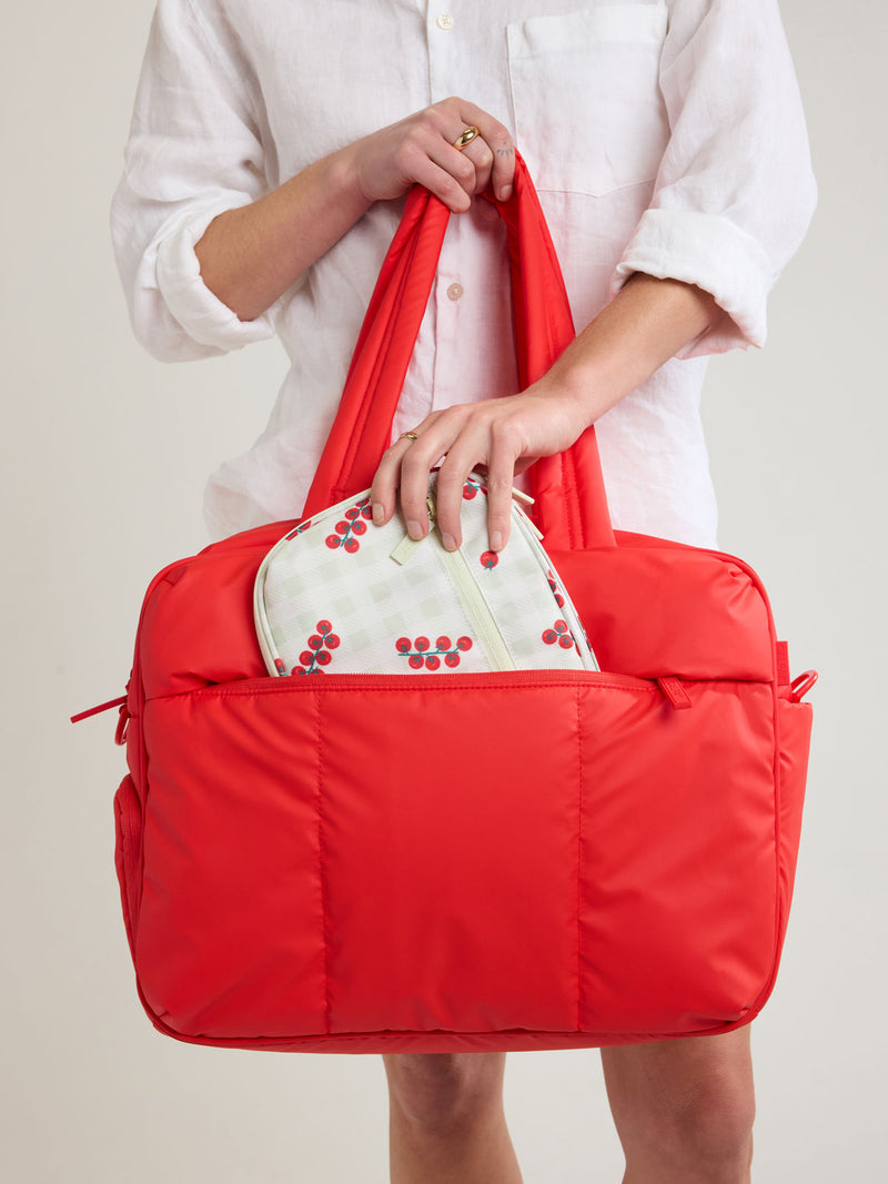 Person putting into a bag the CALPAK Tech Organizer in green and white gingham print with tomato print