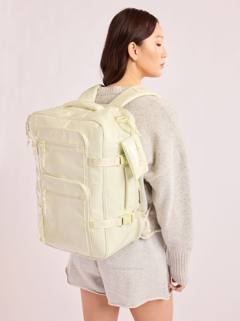 Model in grey wearining the CALPAK Terra 26L Laptop Duffel Backpack with multiple pockets in light green Celadon on a white background