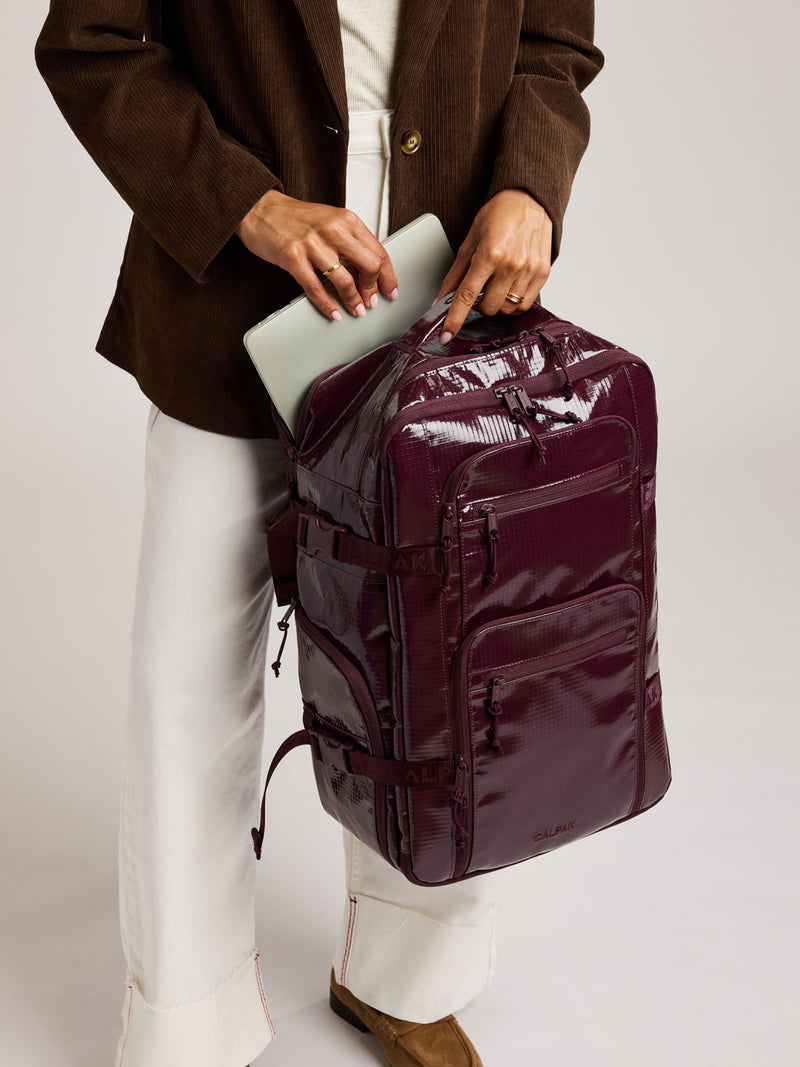 Person holding CALPAK Terra 26L Laptop Backpack in dark red Dark Cherry with multiple pockets on a white background