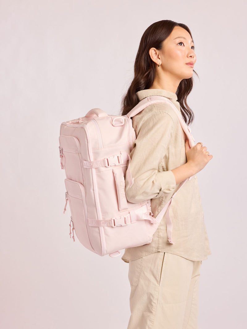 Model waring the CALPAK Terra 26L Laptop Duffel Backpack with multiple pockets in light pink Shell Pink on a white background