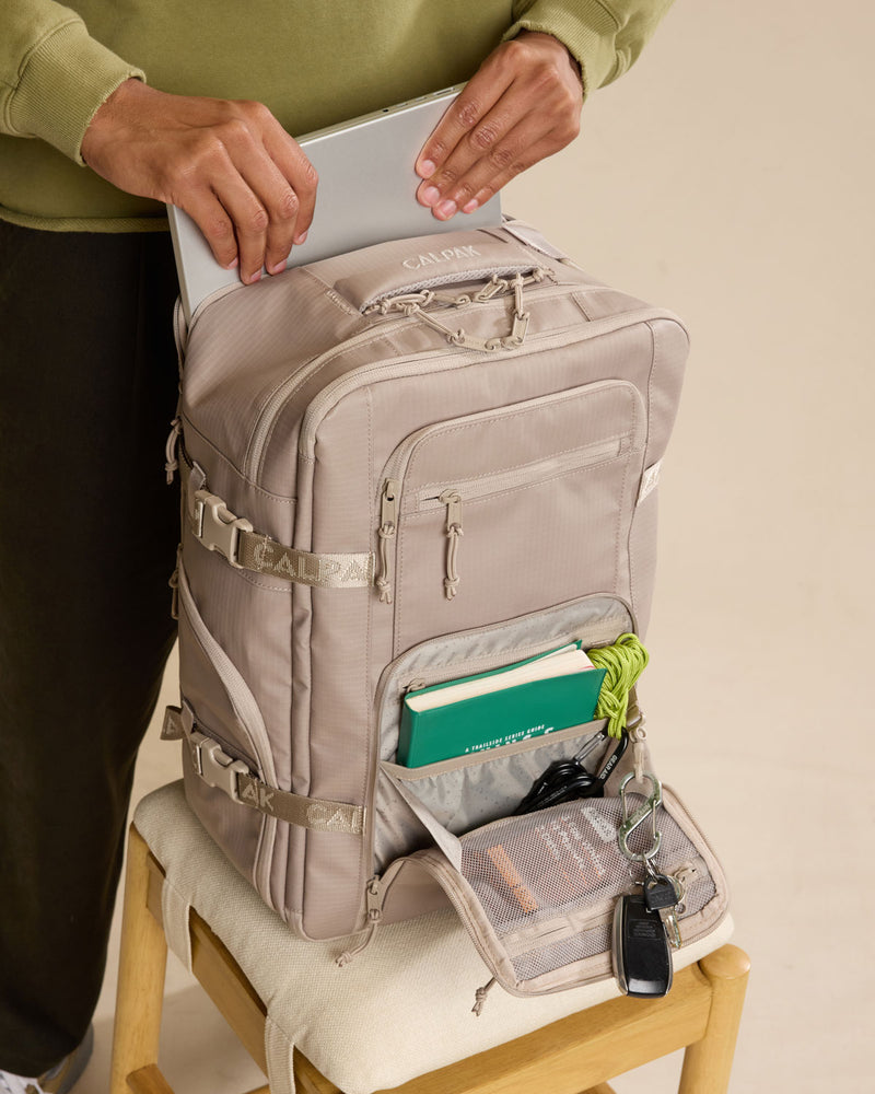 Model putting in laptop into CALPAK Terra 26L Laptop Duffel Backpack in beige Stone front view