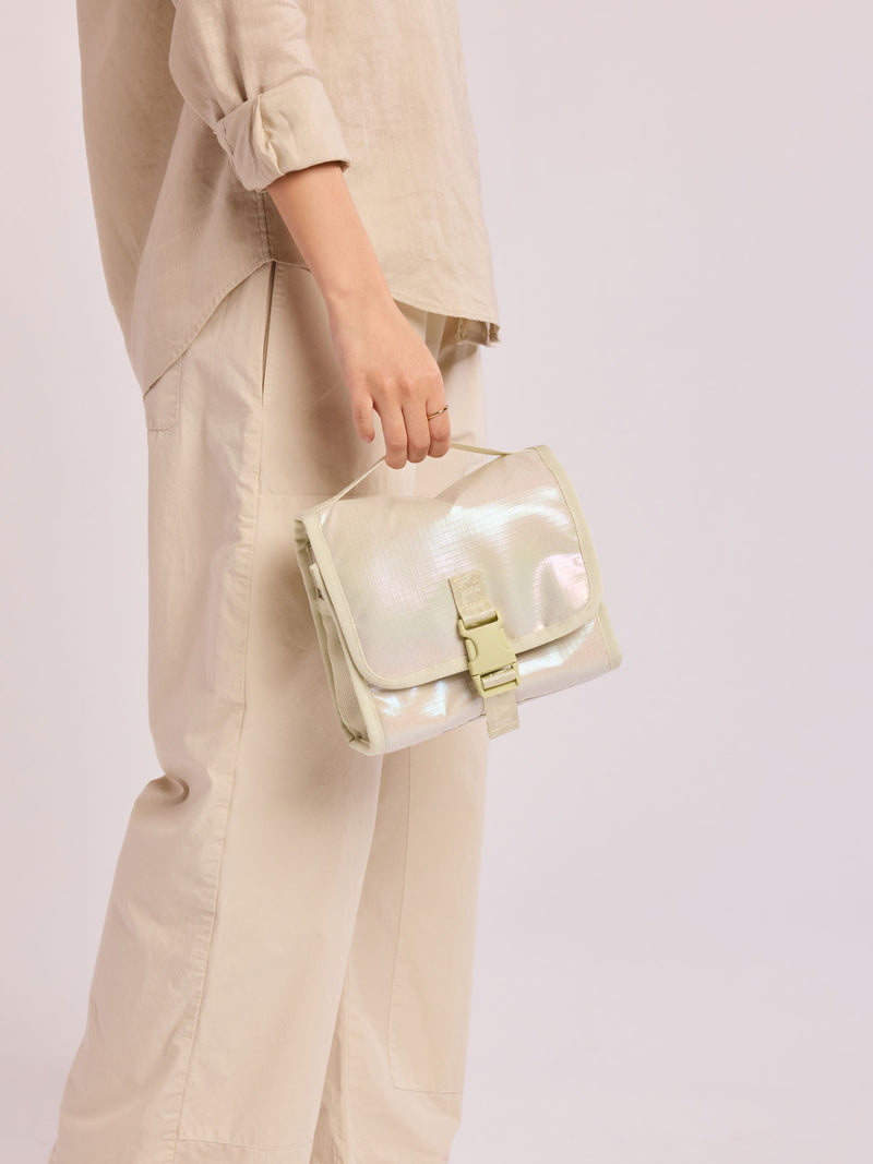 Model holding CALPAK Terra Hanging Toiletry Bag in shiny white Moonbeam with front buckle