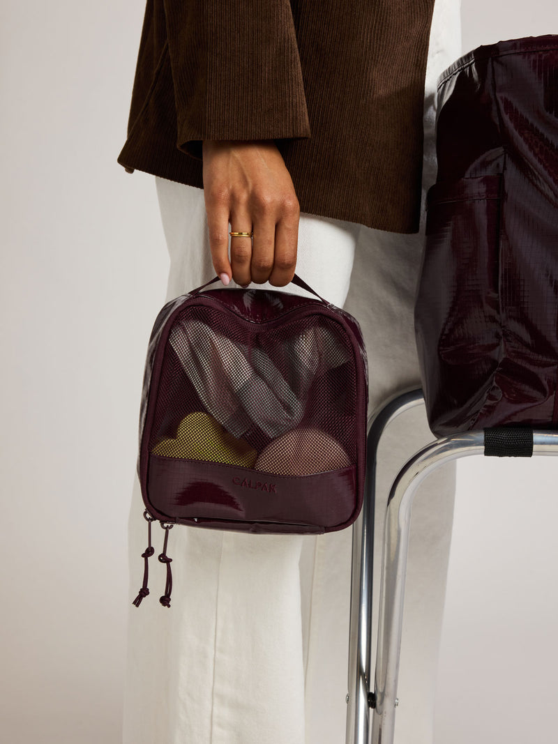 Woman holding the CALPAK Terra 5pc Packing Cube Set in dark red Dark Cherry on a white background