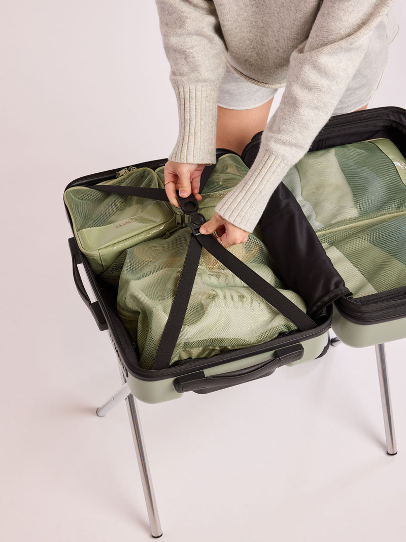 Model packing a suitcase with CALPAK Terra 5-Piece Packing Cube Set in olive green Juniper with two small cubes, two medium cubes, and one large mesh cube with zippers and mesh