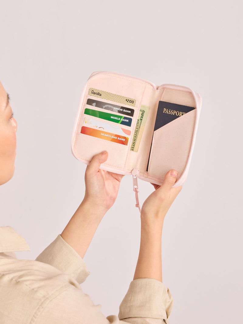 Model holding open the CALPAK Terra Zip Passport Wallet in light pink Shell Pink