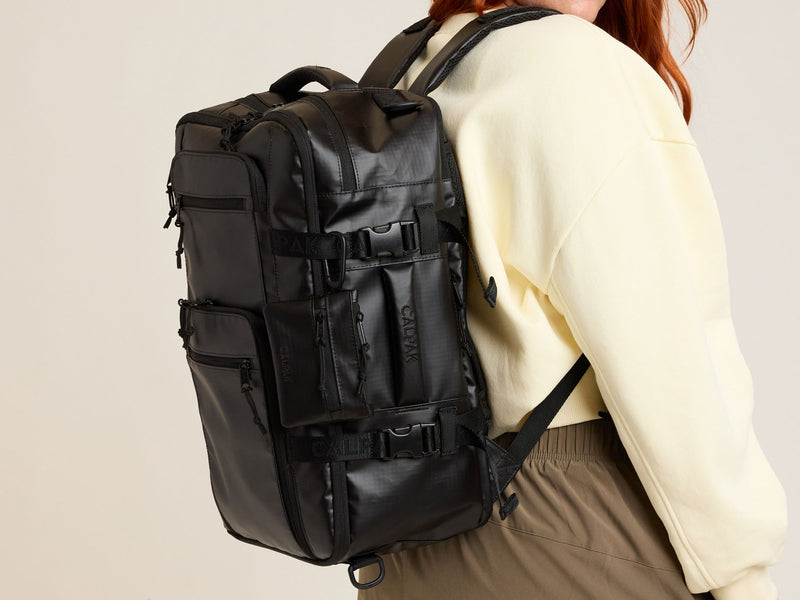 Person wearing a black CALPAK Terra 26L Laptop Duffel backpack on a plain background