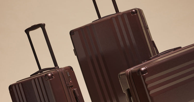 Three CALPAK Ambeur suitcases in Walnut on a beige background