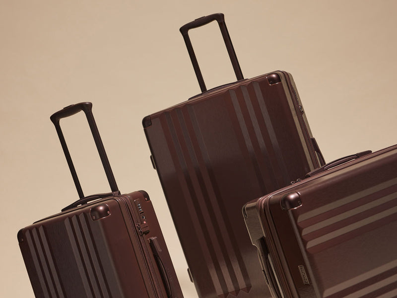 Three CALPAK Ambeur suitcases in Walnut on a beige background