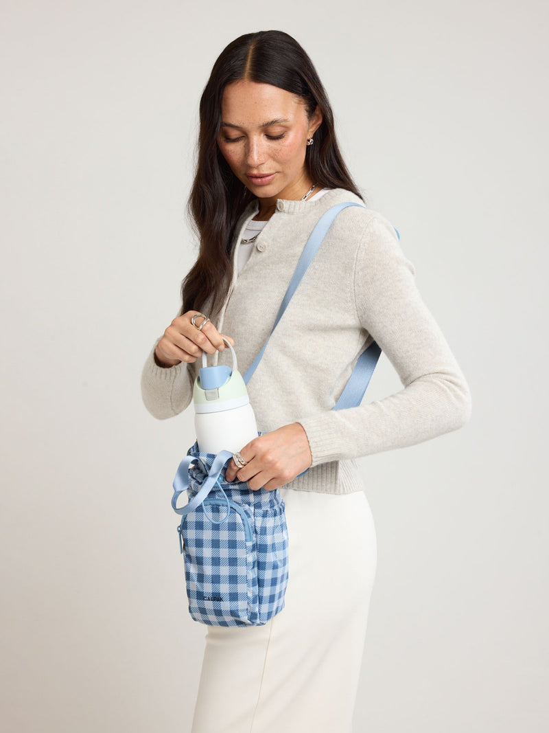 Woman putting a water bottle in the CALPAK Water Bottle Holder in blue and white checkered French Blue Gingham