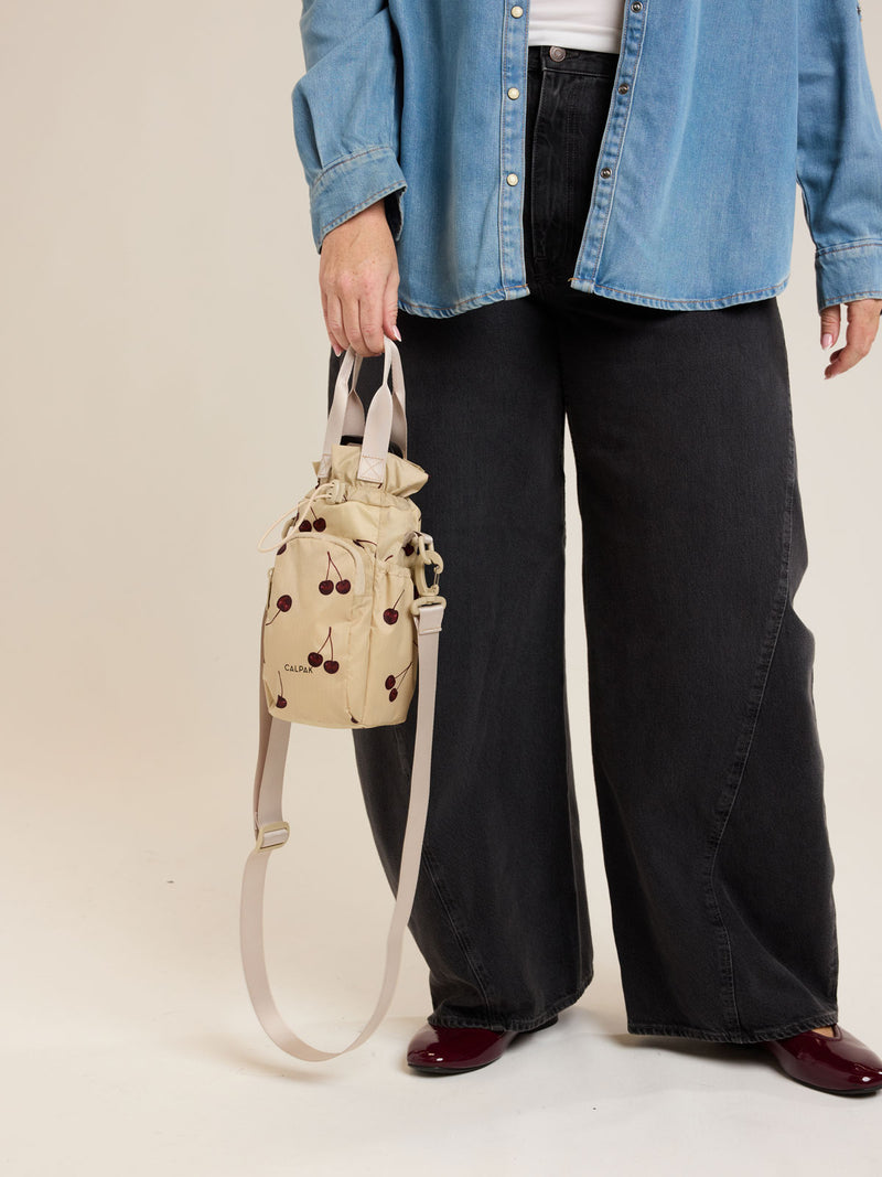 Model holding CALPAK Water Bottle Holder in Oatmeal Chery in beige with cherry pattern