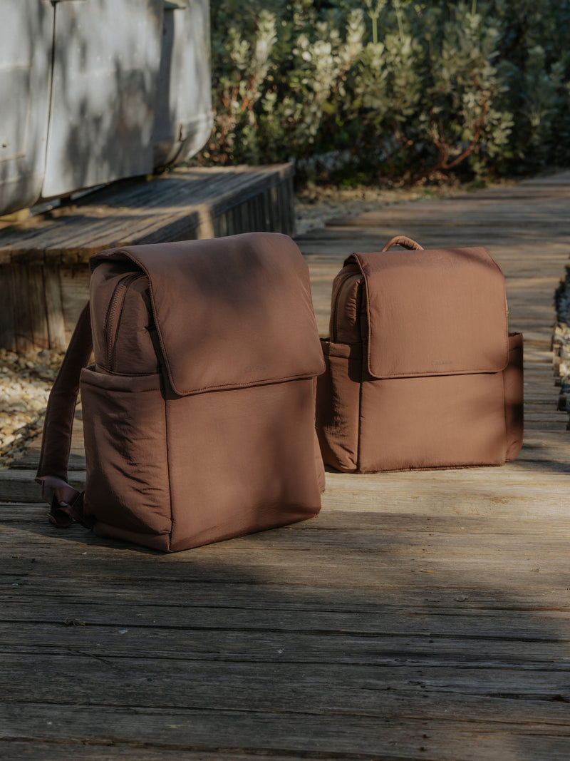 CALPAK Diaper Backpack and  Mini Diaper Backpack in brown Hazelnut in a nature background