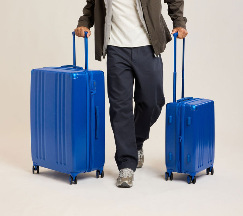 Person holding two blue Ambeur 2-piece suitcases against a plain background