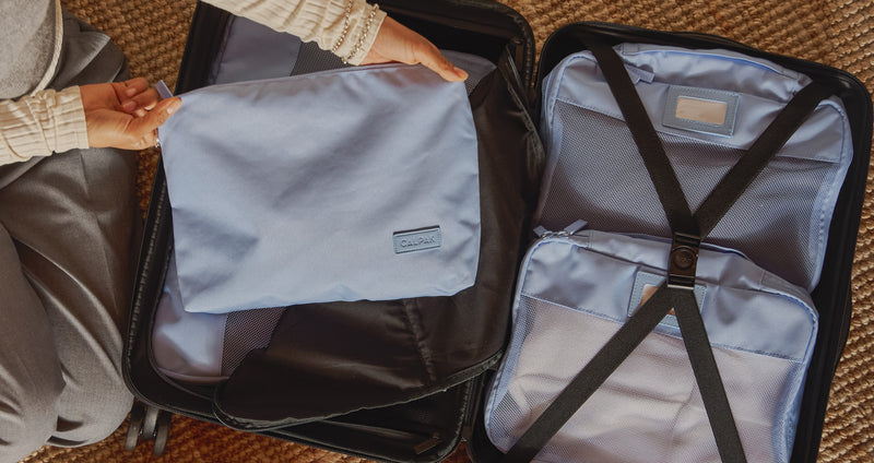 Person packing a suitcase using light blue CALPAK packing cubes
