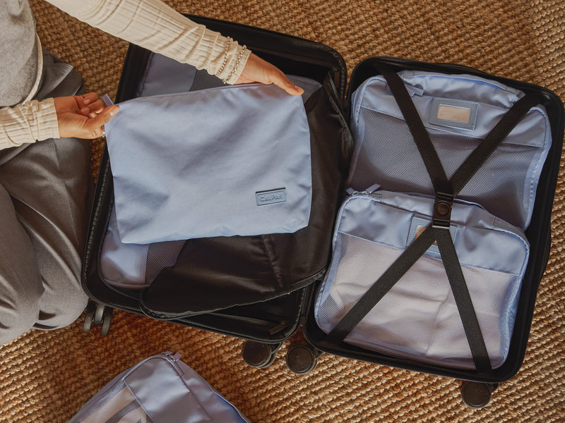 Person packing a suitcase using light blue CALPAK packing cubes