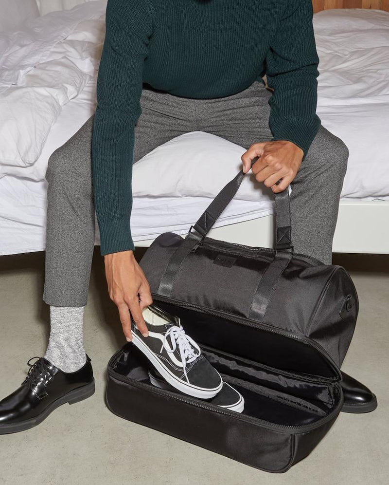 The Stevyn Duffel Bag in black, featuring a front zippered pocket, top handles, and an adjustable shoulder strap. The spacious duffel is ideal for travel, gym, or weekend trips, offering both style and functionality