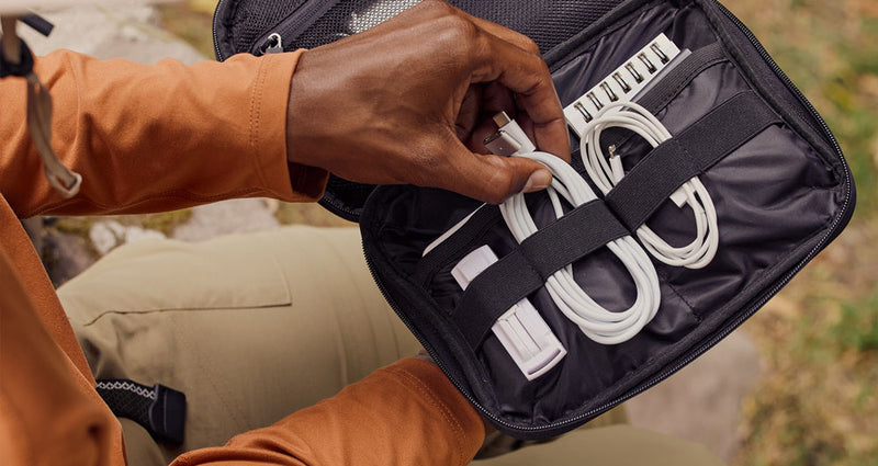 Model placing laptop charger and phone charger in the CALPAK Tech Organizer in Black